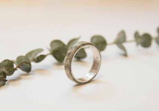 Anillo de papel con plata por dentro visto de lado. Se ve el grabado que se le puede añadir al interior